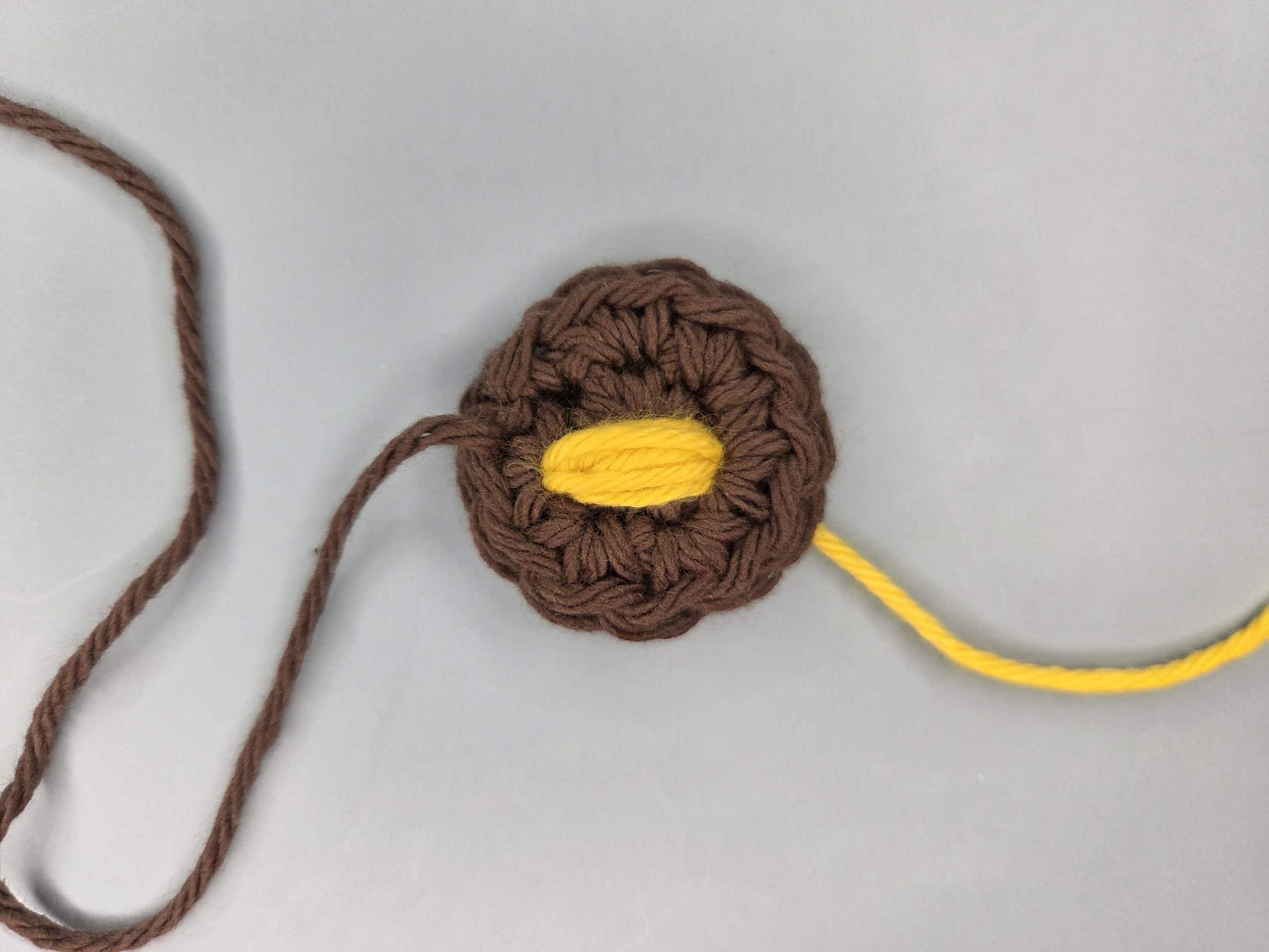 Brown crochet circle with yellow horizontal satin stitch embroidery forming the bee body in the center.
