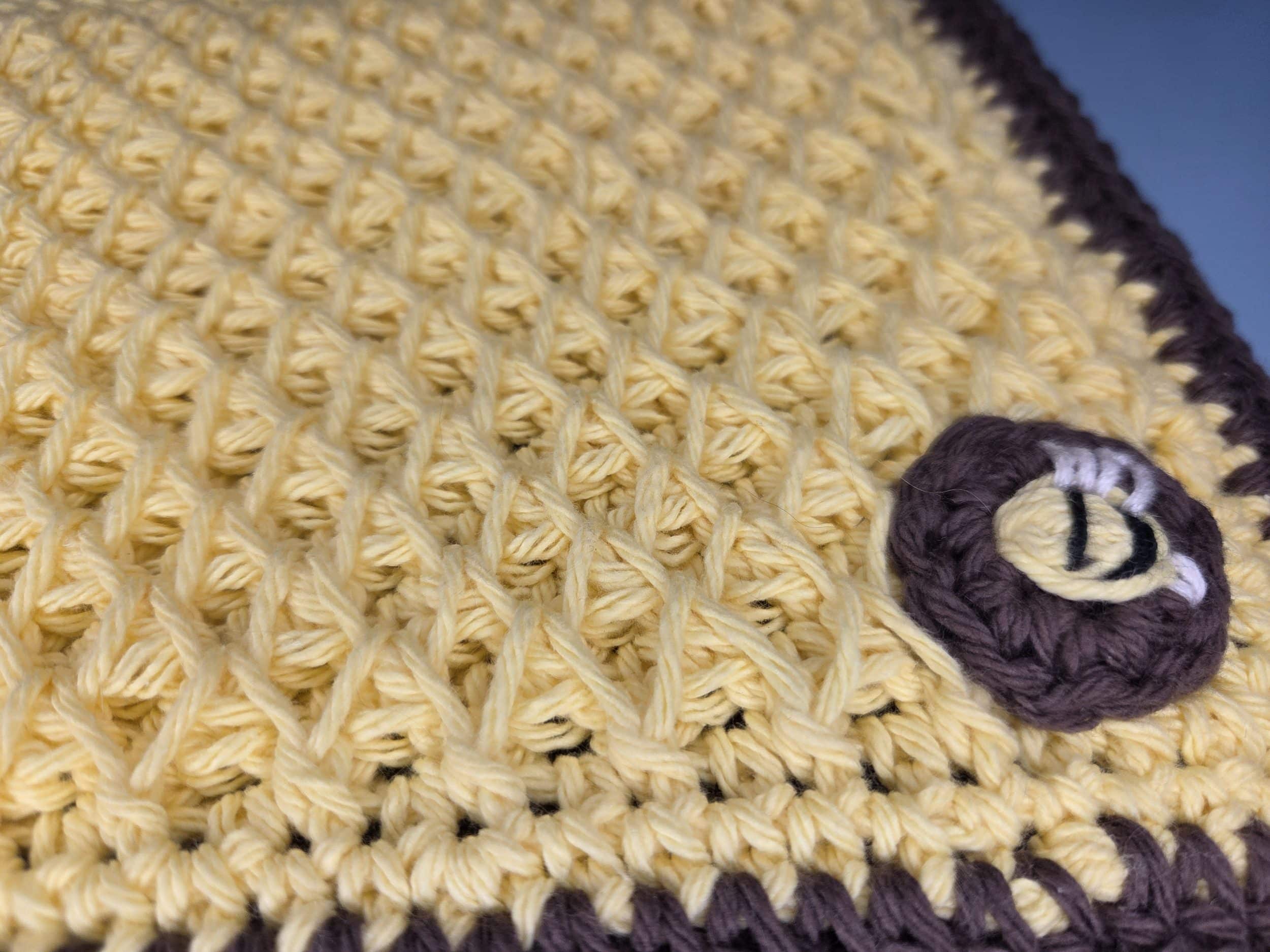 Close up of yellow crochet smock stitch hot pad with brown hdc border and small embroidered bee circle with white wings and black stripes sewn onto the corner.