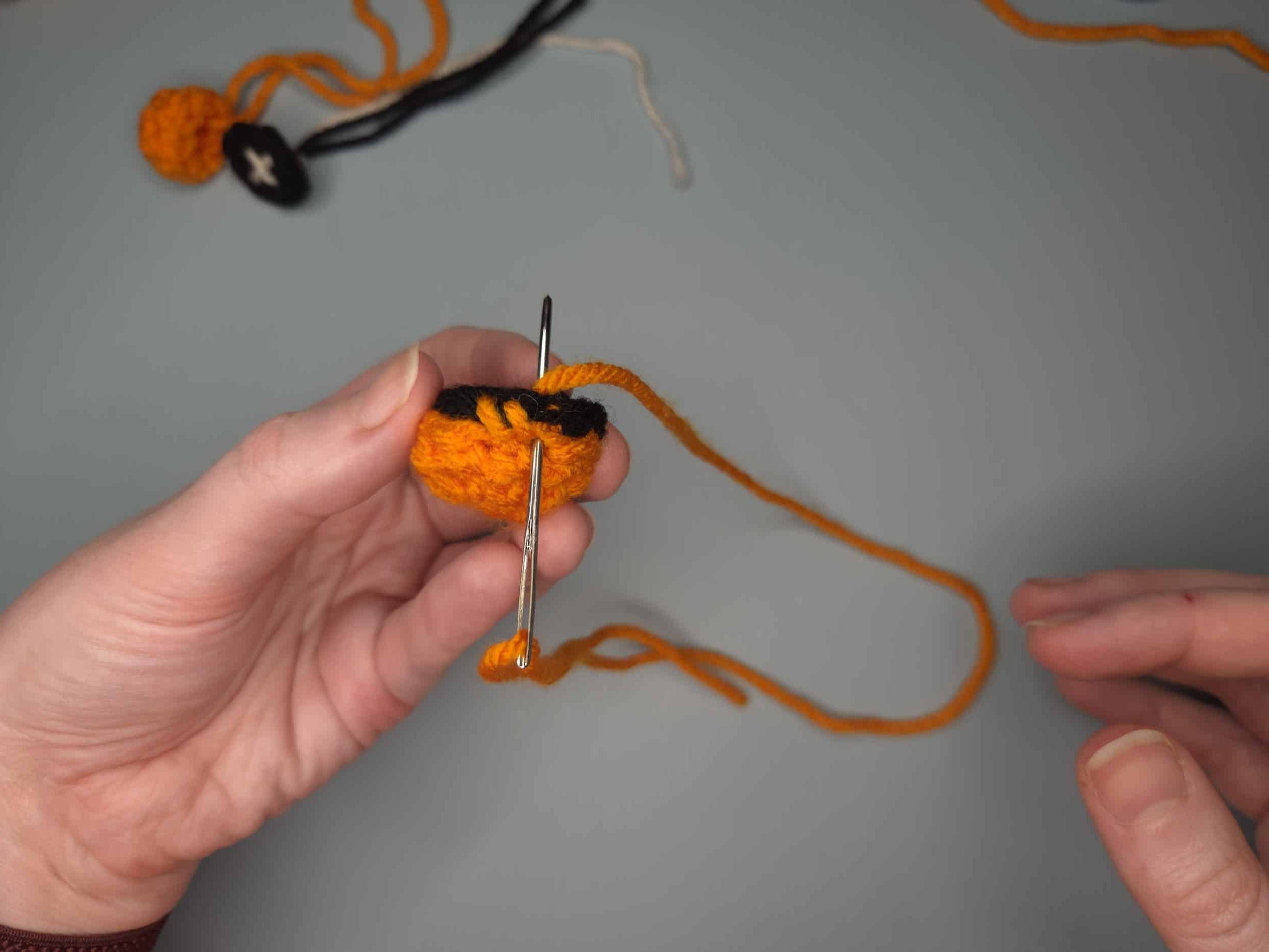 Hands whip stitching the white eye front onto the black and orange crochet eye back using a tapestry needle and orange yarn.